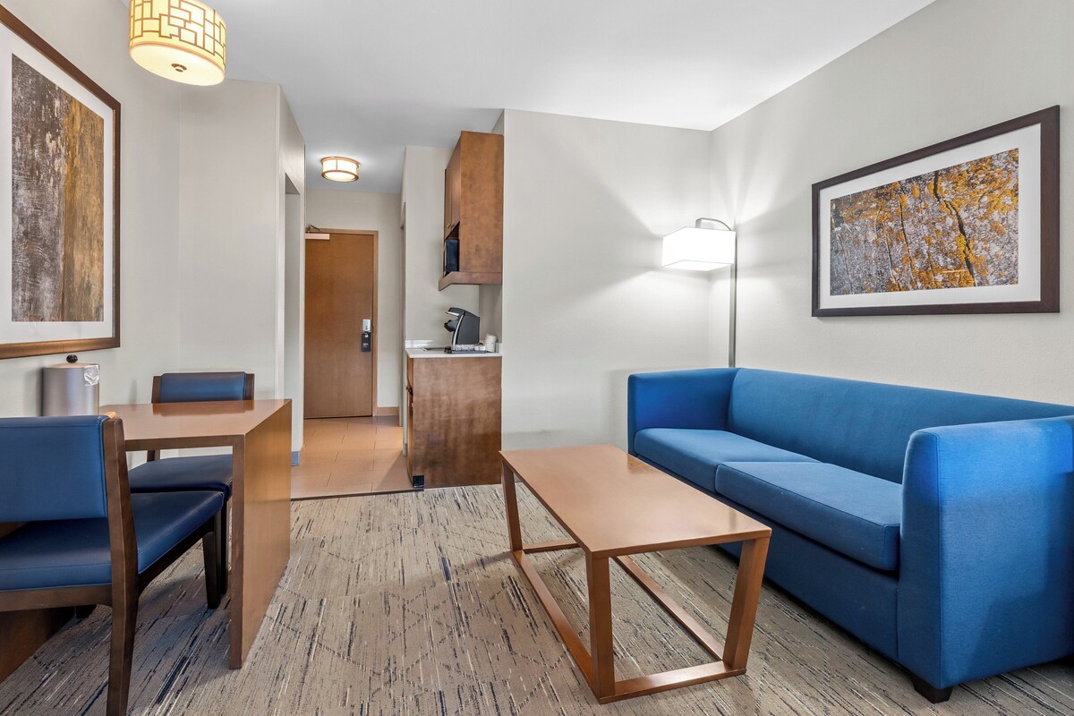 Ein modernes Hotelzimmer mit einem blauen Sofa, einem Holztisch und einem Essbereich mit Tisch und Stühlen.