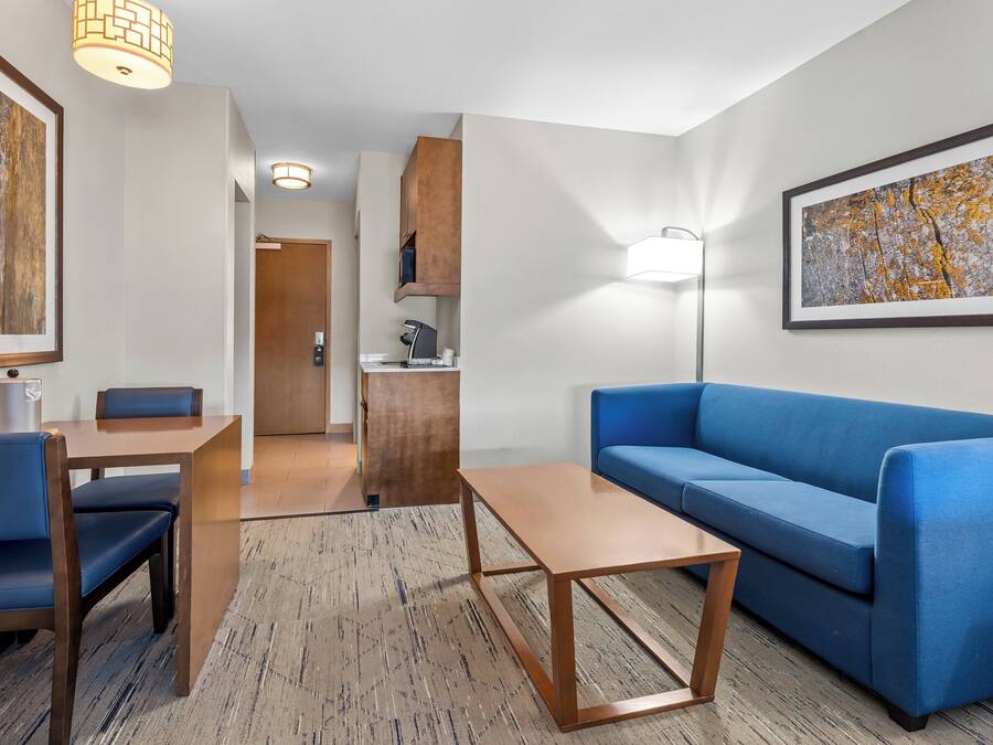 A modern hotel room with a blue sofa, wooden coffee table, and a dining area with a table and chairs.