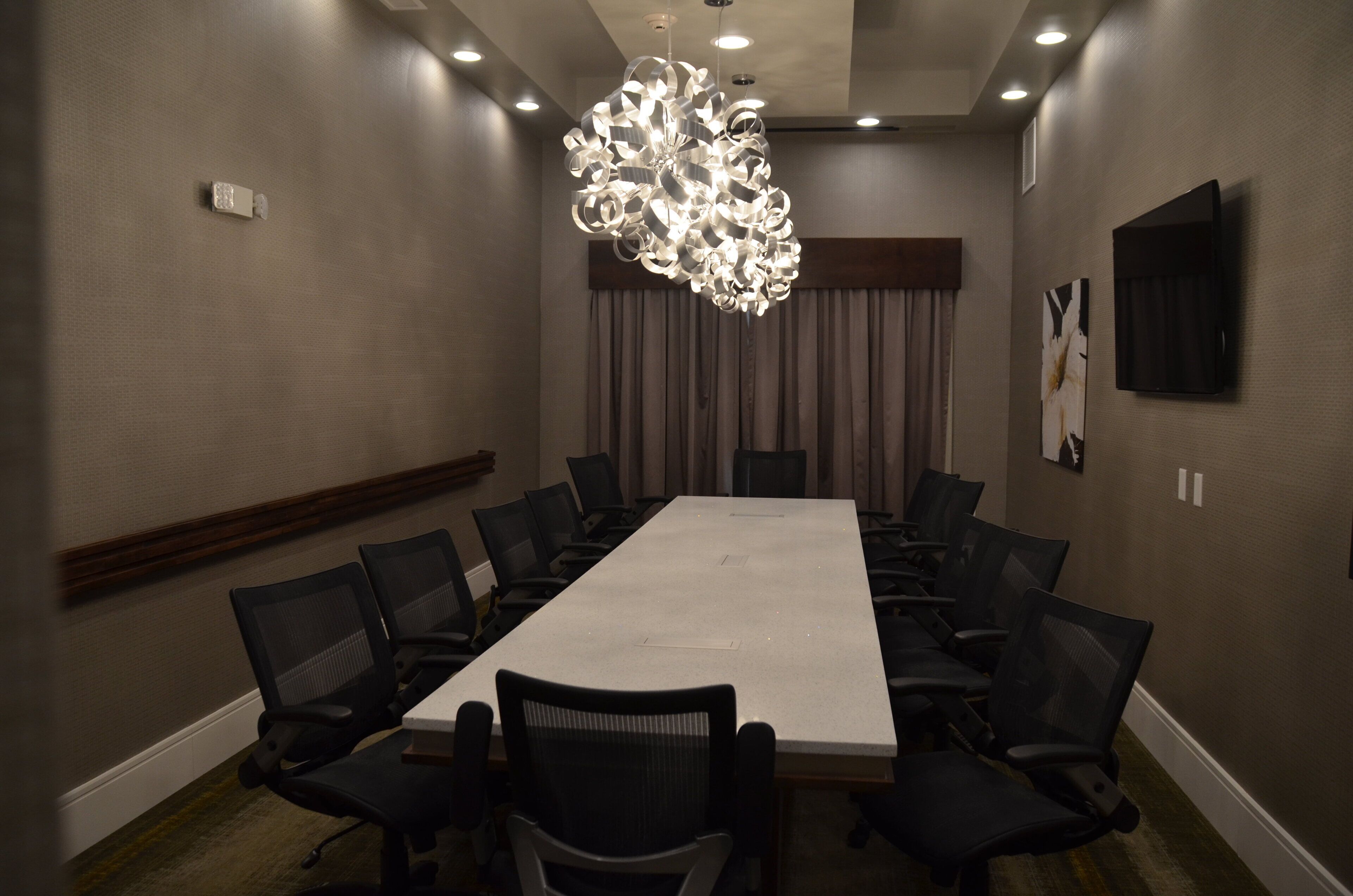 A conference room with a long table, chairs, a modern chandelier, and a television on the wall.