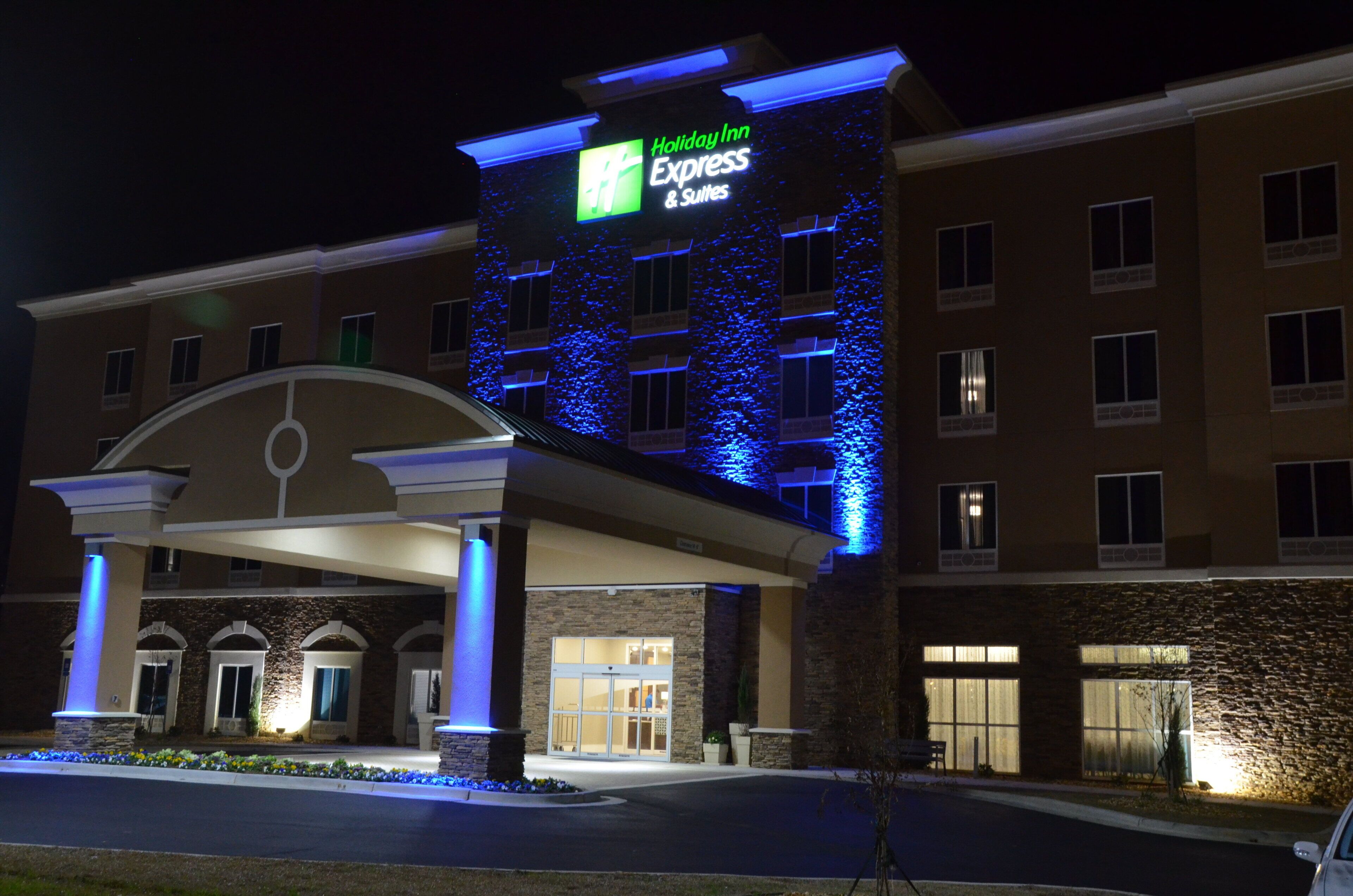 A Holiday Inn Express & Suites building with a modern design, featuring a prominent entrance with a covered walkway and a sign displaying the hotel name.