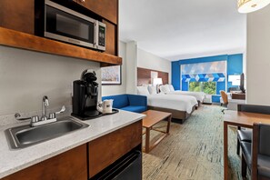 Ein Hotelzimmer mit Kochnische, einem Bett, einem blauen Sofa, einem Schreibtisch und Blick auf Grünflächen.