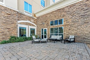 Un patio con muros de piedra, mobiliario exterior y grandes ventanales.