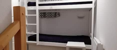 A bunk bed room with a wooden ladder, a small white table, and a radiator.