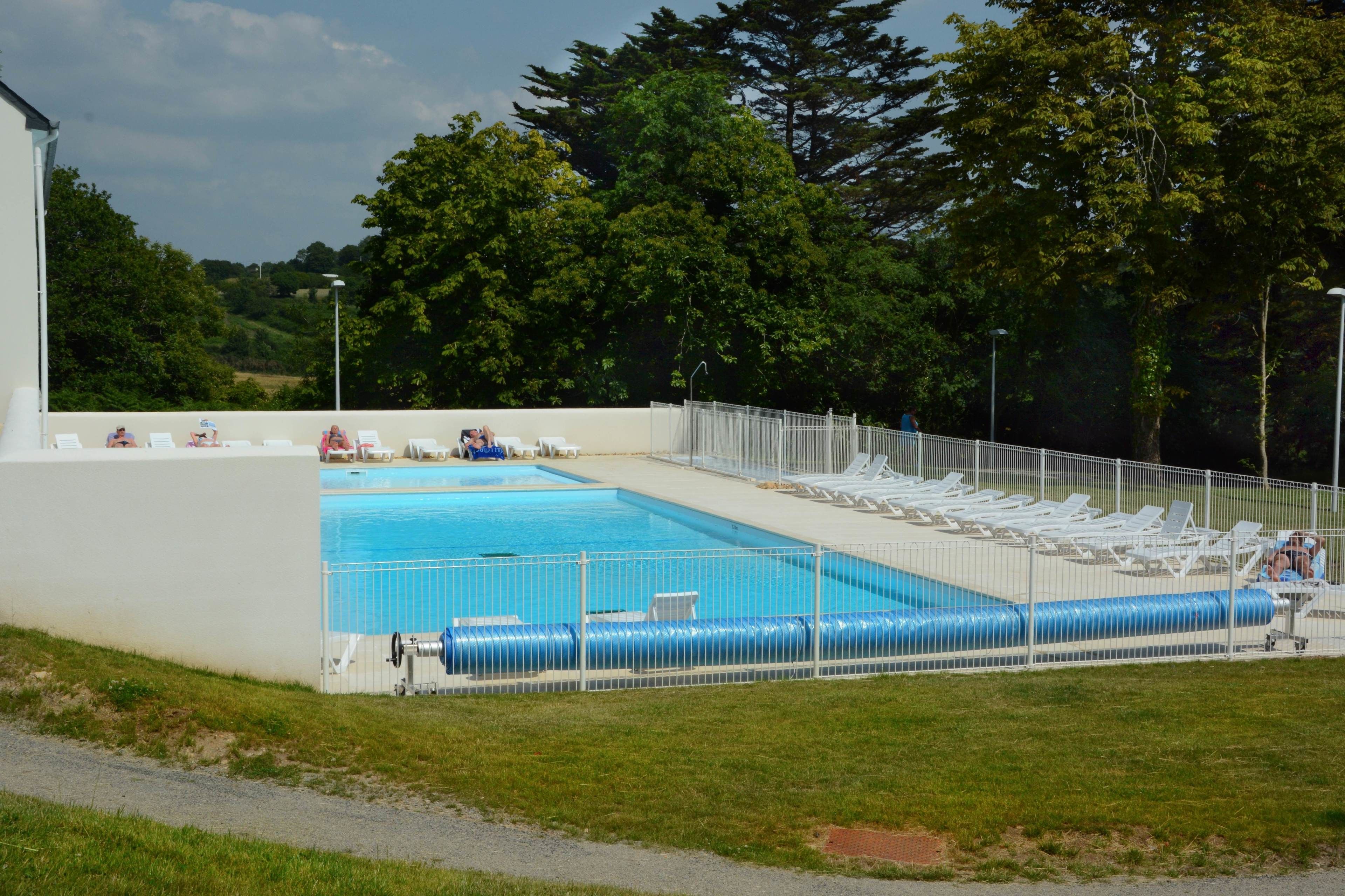 Una piscina con una zona de terraza cercada, rodeada de árboles y un cielo despejado.