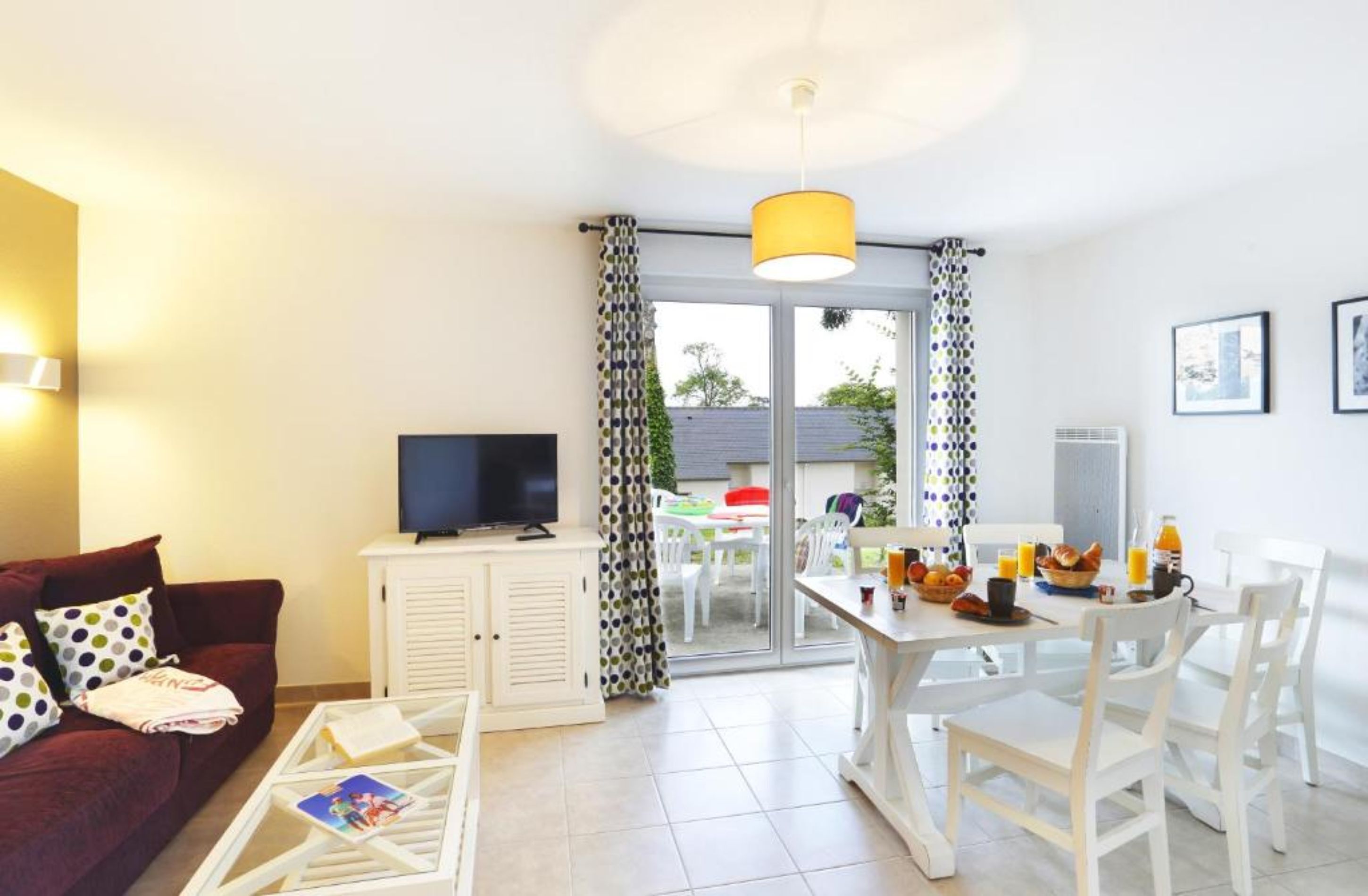 Un salon comprenant un canapé, un téléviseur et un coin repas avec une table et des chaises.