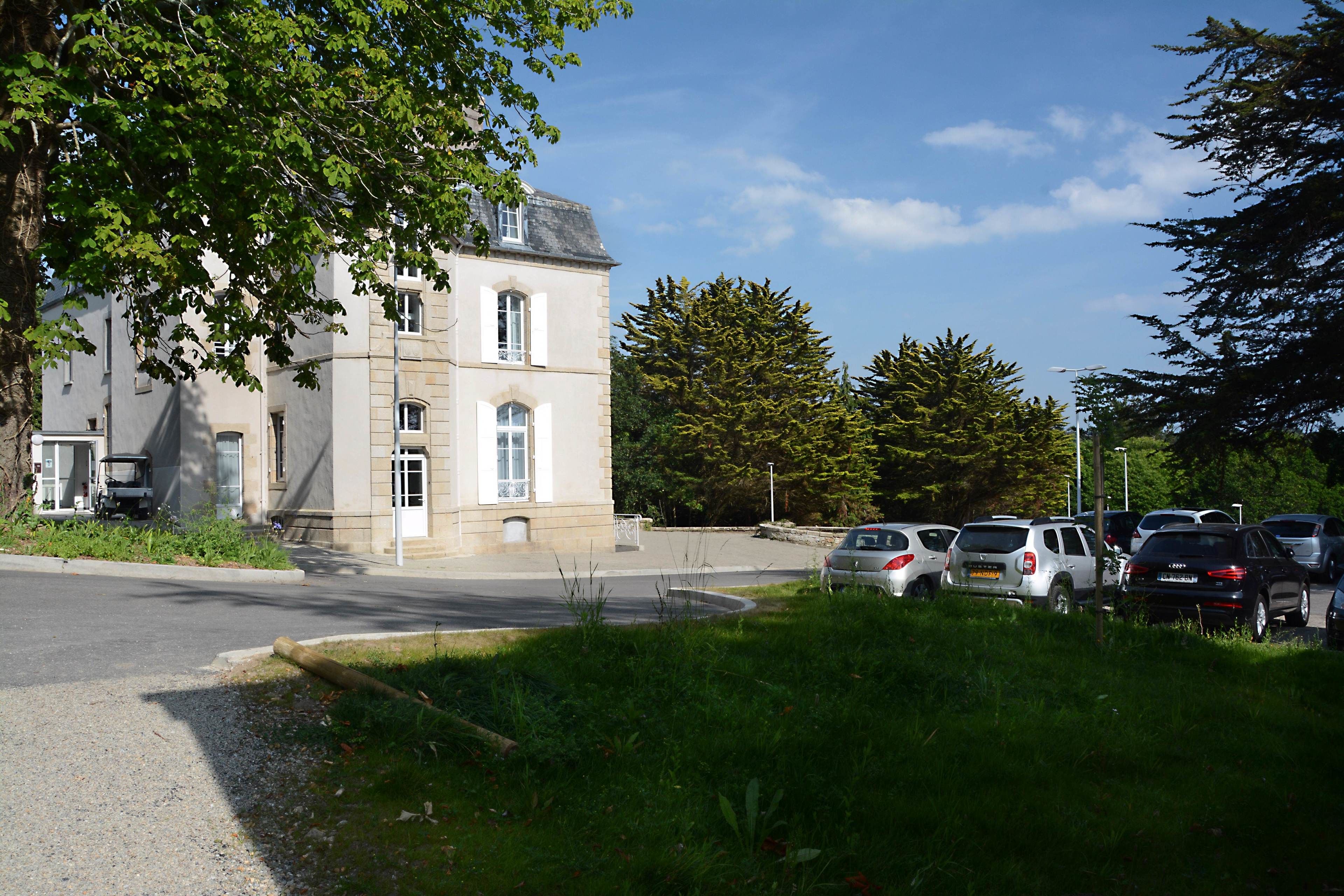 A building with a stone facade, parked cars, and a grassy area in front.
