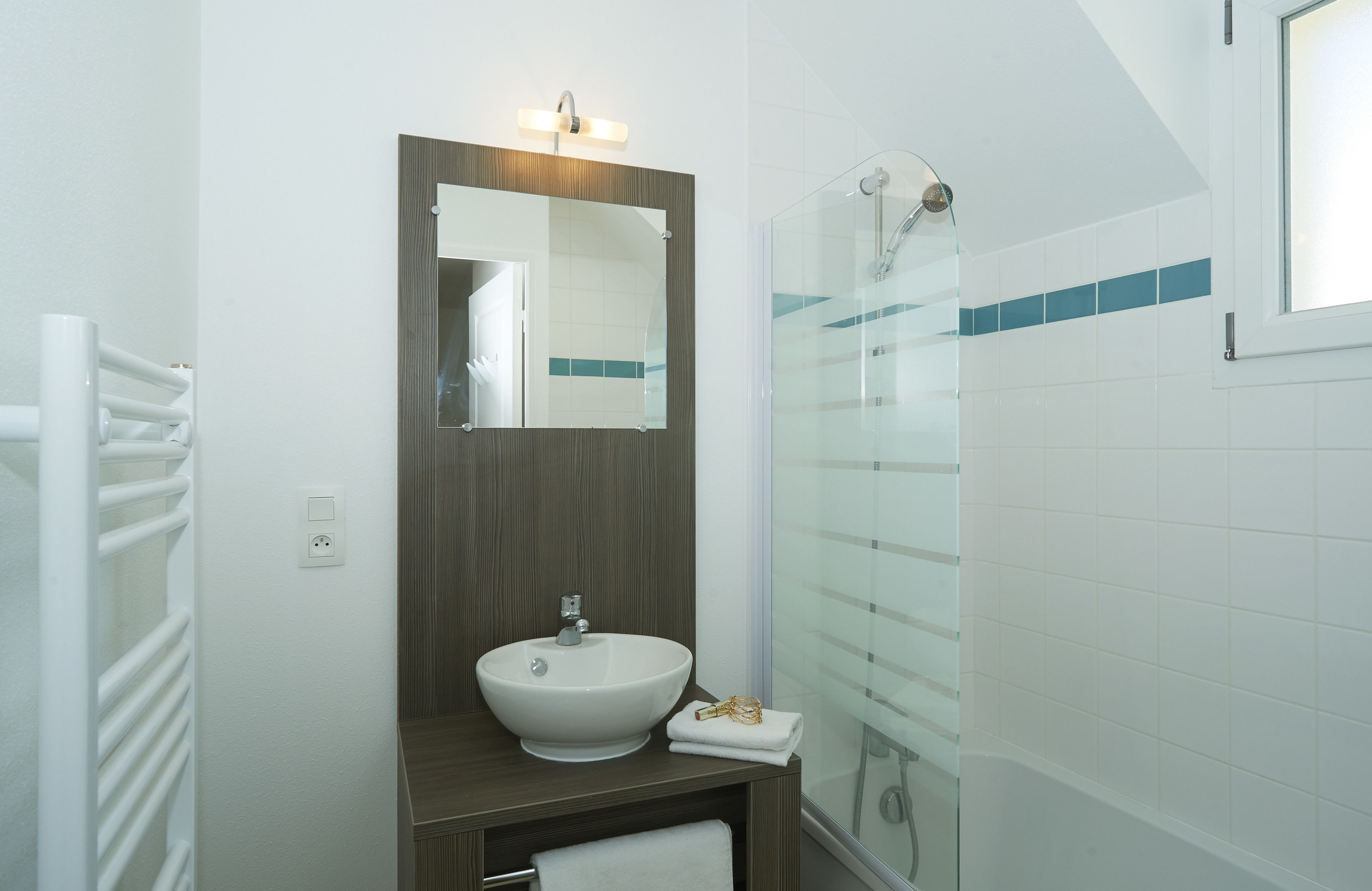 Une salle de bain moderne avec un lavabo blanc, un miroir et une cabine de douche en verre.