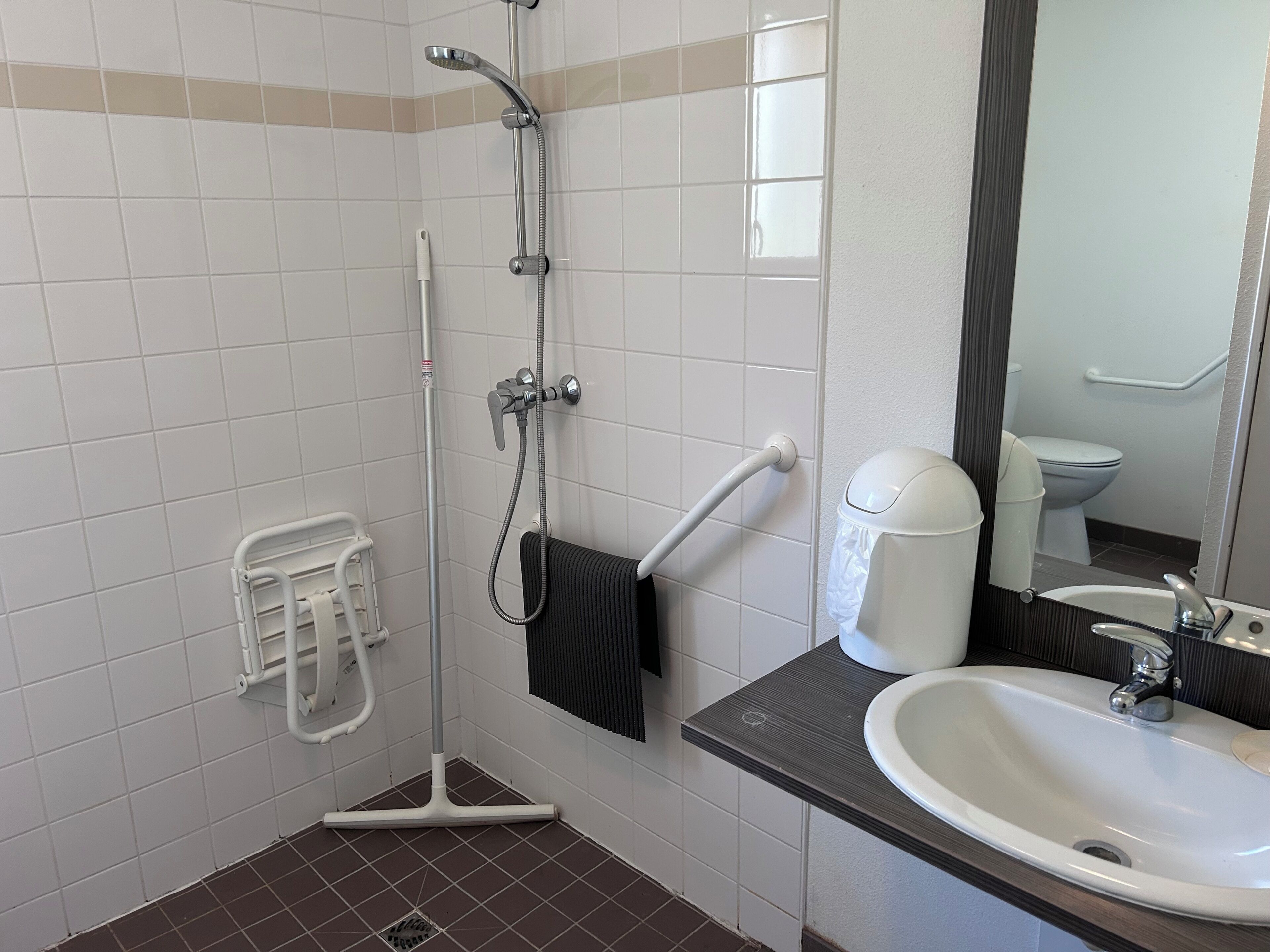 Un baño con ducha, lavamanos, inodoro y secamanos.