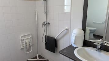 Un baño con ducha, lavamanos, inodoro y secamanos.