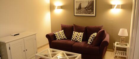 A living room with a brown sofa, white side table, and a glass coffee table.