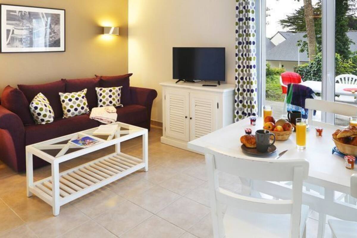A living room with a sofa, coffee table, TV, and dining table set with breakfast items.