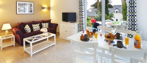A living room with a sofa, coffee table, TV, and dining table set with breakfast items.