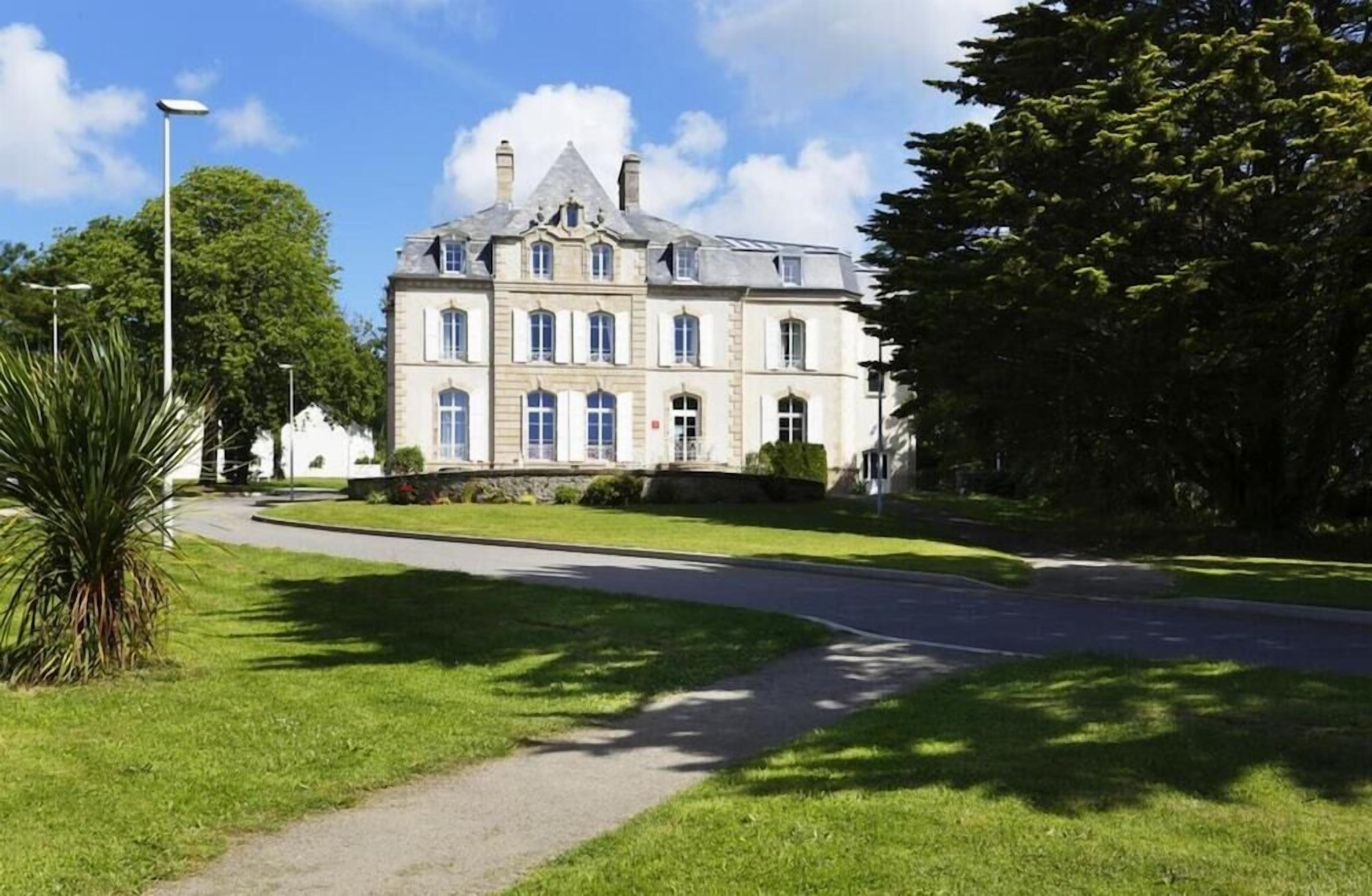 A large, historic building with symmetrical architecture, a central entrance, and a well-maintained lawn.