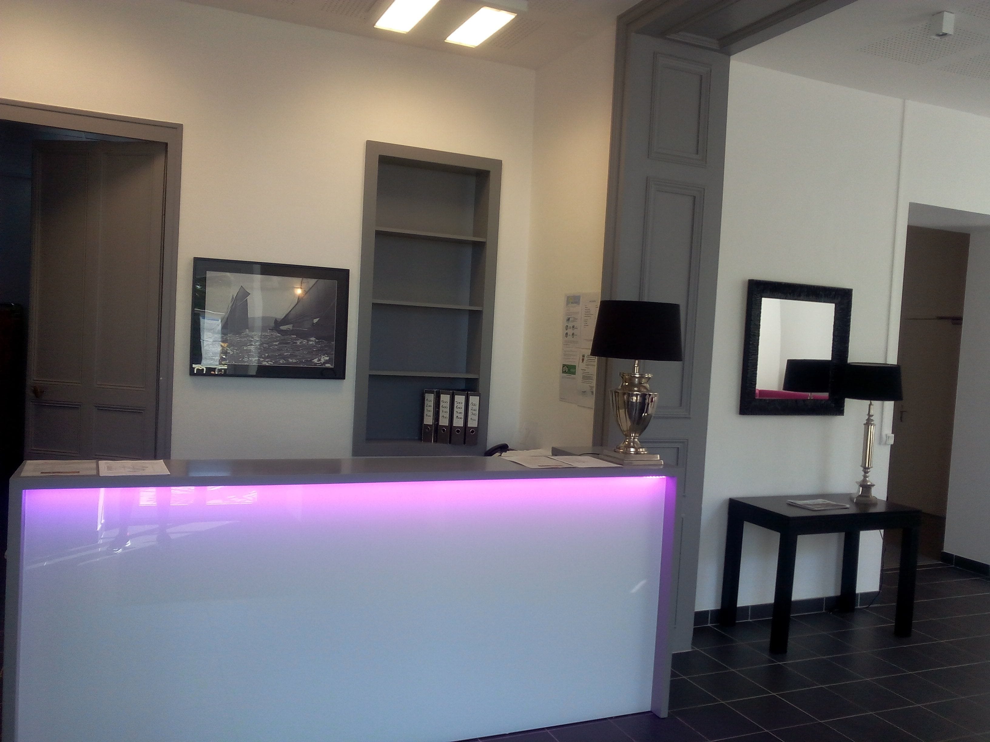 A reception desk with a purple-lit counter, a framed picture, a lamp, and a mirror on the wall.