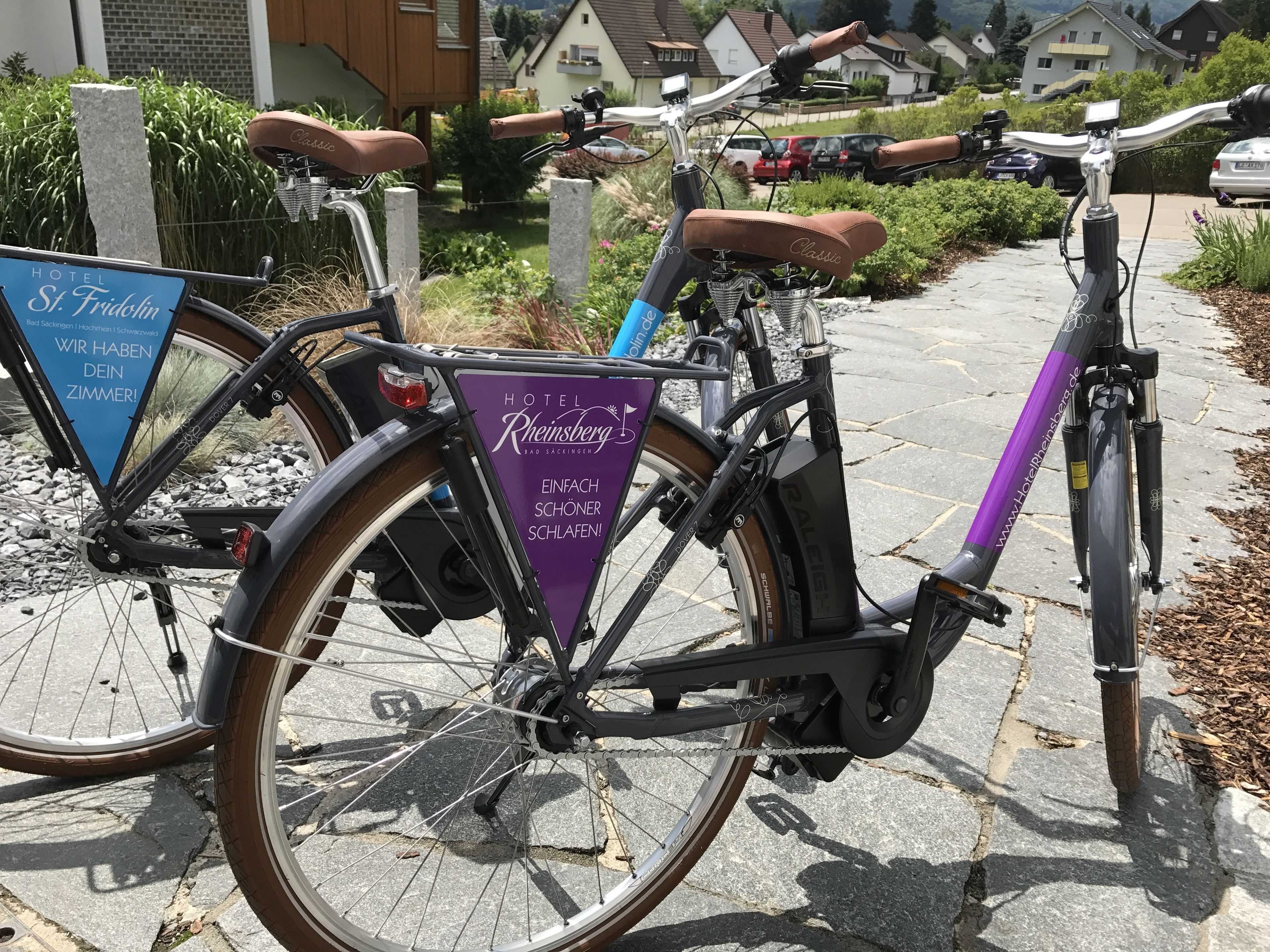 A bicycle with a purple sign attached, parked on a stone pathway.