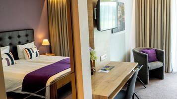 Una habitación de hotel con una cama, un escritorio, una silla, un televisor y cortinas.