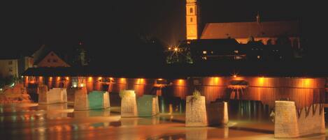 Un edificio histórico con una torre destacada, un patio con agua reflectante y una serie de estructuras iluminadas.
