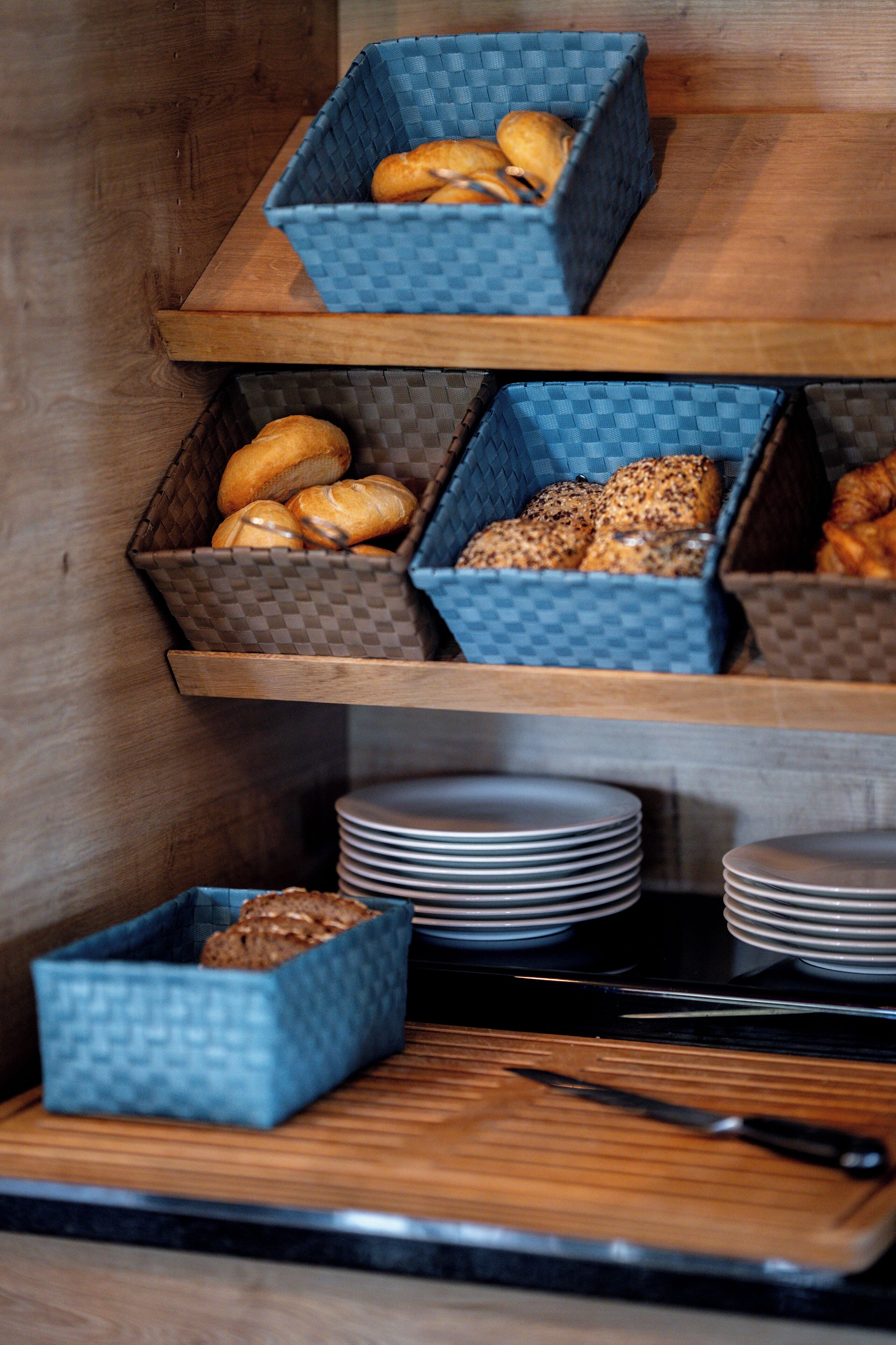 A kitchen counter with three blue baskets containing bread, stacked plates, and a knife.