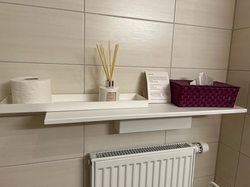 Un baño con un estante blanco que contiene papel higiénico, un difusor de cañas y una caja de pañuelos.