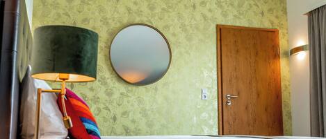 Une chambre d’hôtel avec un lit, un miroir rond, une porte en bois et une lampe.