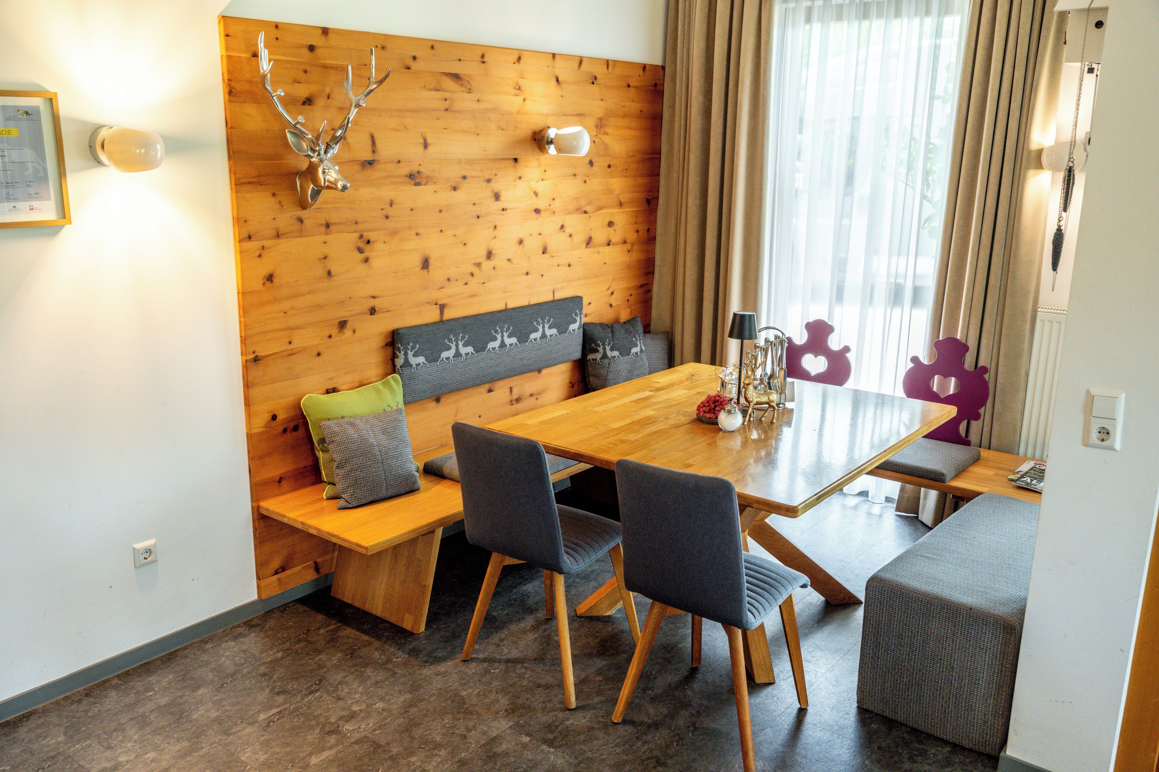 Un comedor con una mesa de madera, sillas tapizadas de gris y un banco con cojines estampados.