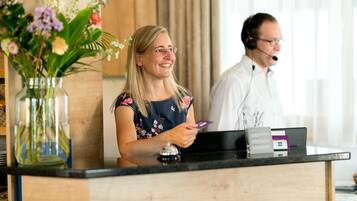A reception desk with a vase of flowers, a black counter, and a man in a headset.