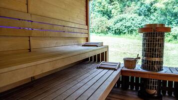 Un sauna en bois, doté de bancs, d’un appareil de chauffage et d’une fenêtre donnant sur la verdure.