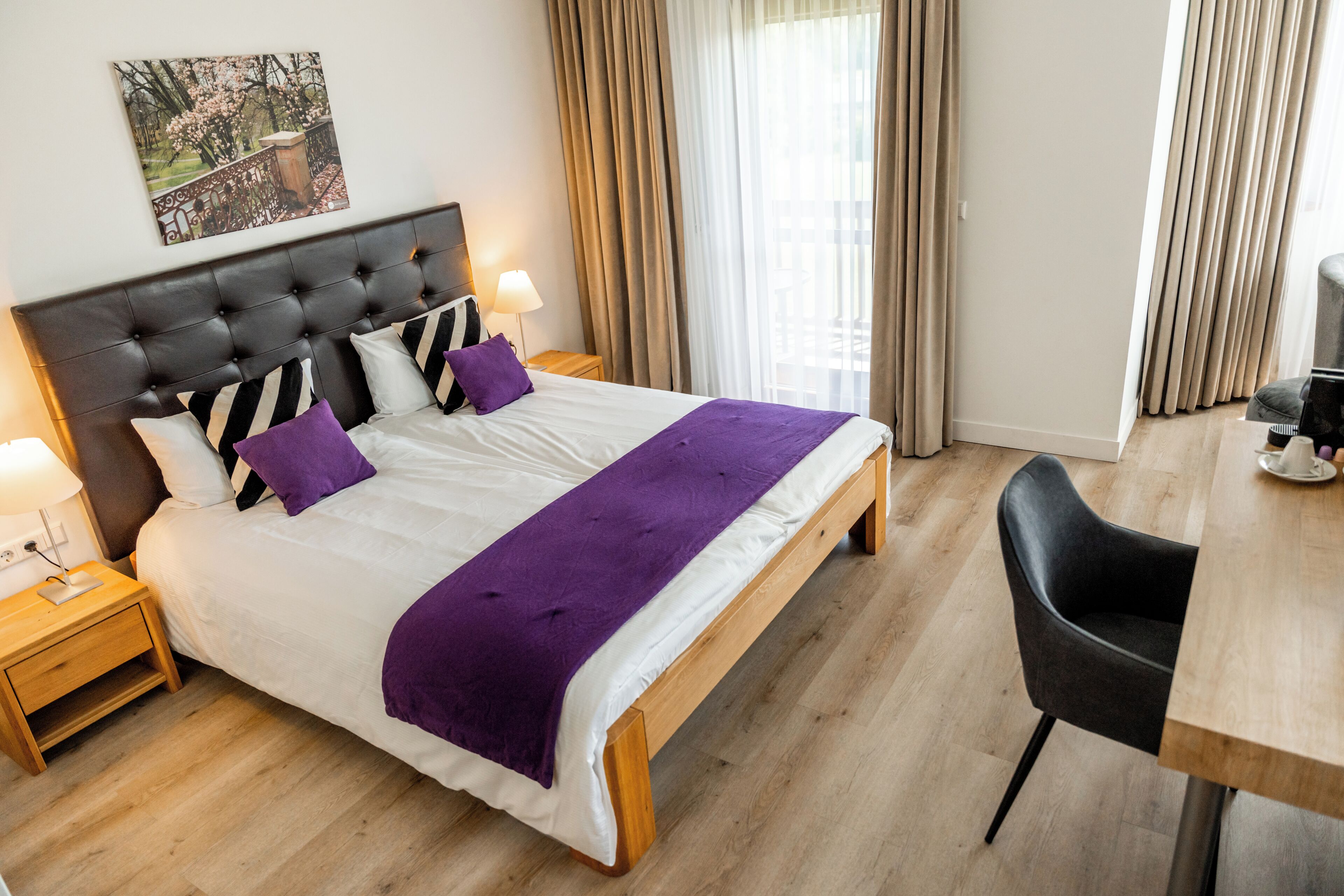 Una habitación de hotel con una cama grande, cabecera de madera, dos mesitas de noche con lámparas, un escritorio de madera y una silla.