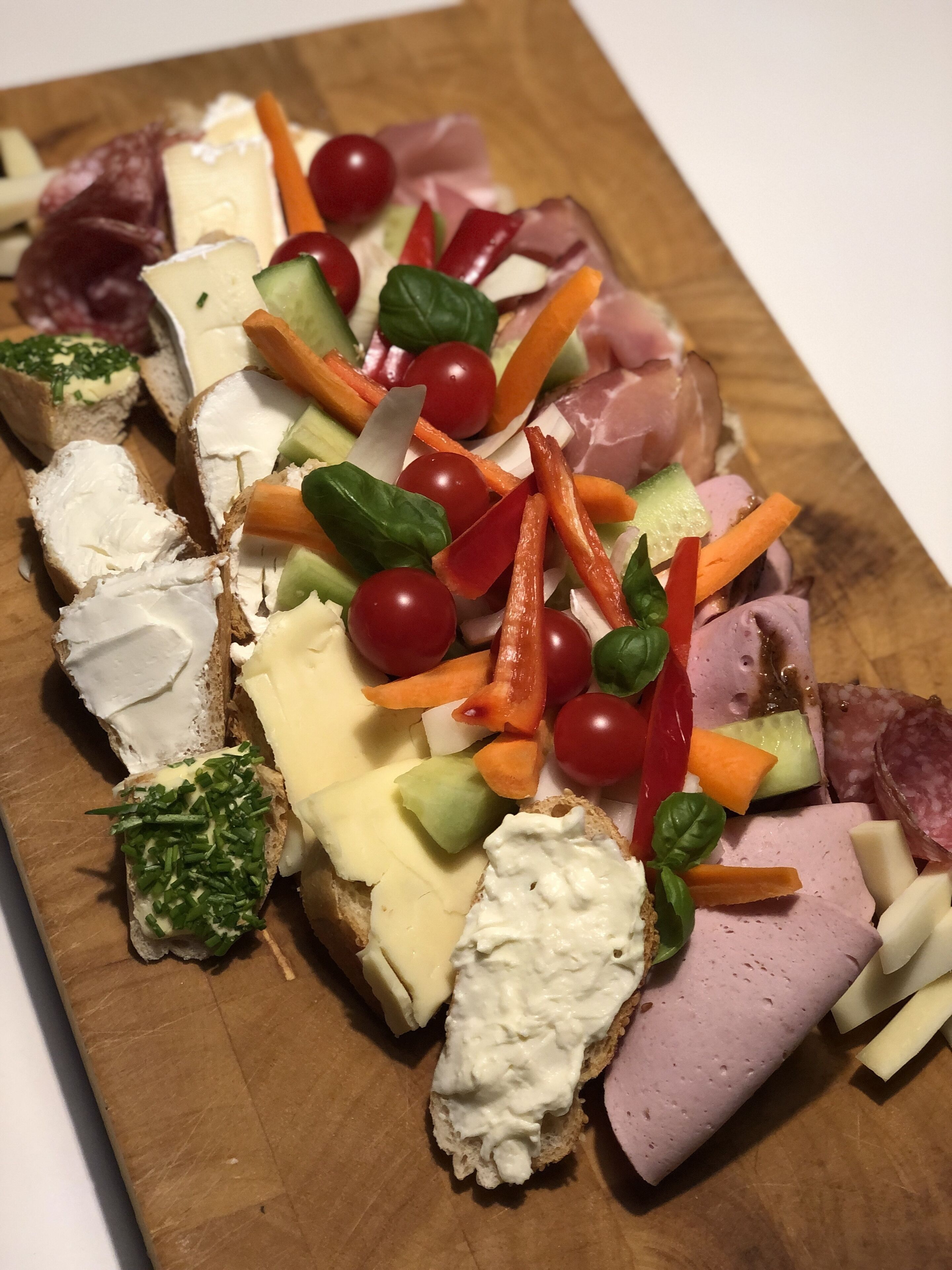 A wooden board with various cheeses, meats, and vegetables arranged for a charcuterie board.