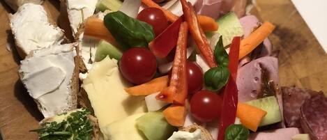 A wooden board with various cheeses, meats, and vegetables arranged for a charcuterie board.