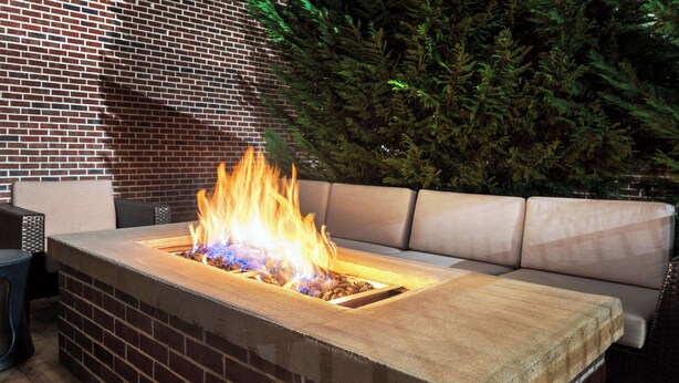 Un elemento decorativo a forma di rettangolo con fiamme, un muro in mattoni e un albero verde sullo sfondo.