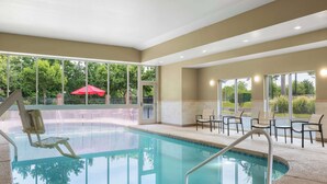 Una piscina coperta con pareti in vetro trasparente, una sedia a bordo piscina e diverse sedie disposte nell'area della piscina.
