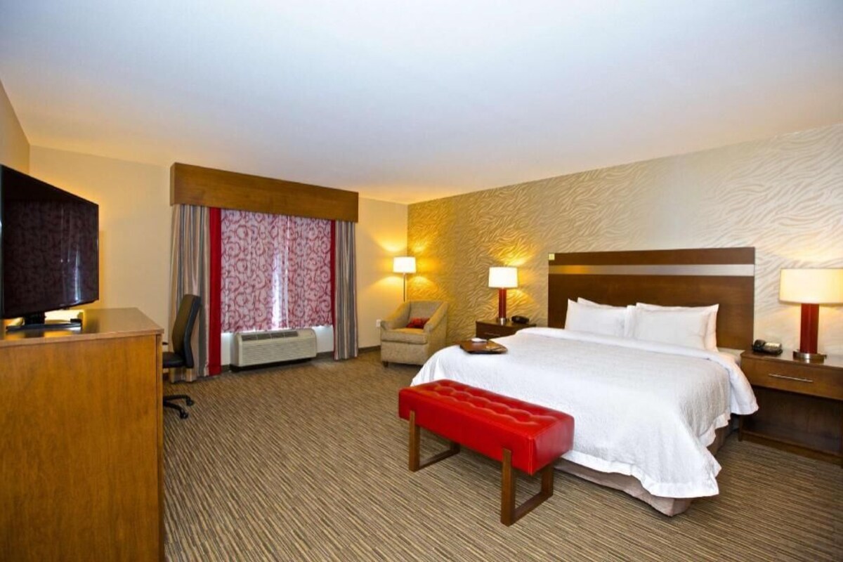 Hotelkamer met een bed, bedlampen, een bureau, een televisie, een stoel en een raam met gordijnen.