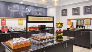 Un'area colazione con un cartello che indica l'inizio della colazione, un espositore di muffin e una bancarella di frutta.