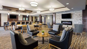 A hotel lobby with a dining area, seating area, and a TV mounted on the wall.