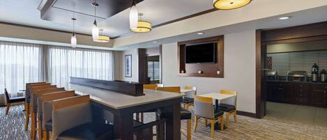 A hotel room with a dining area, a TV mounted on the wall, and a kitchen area.