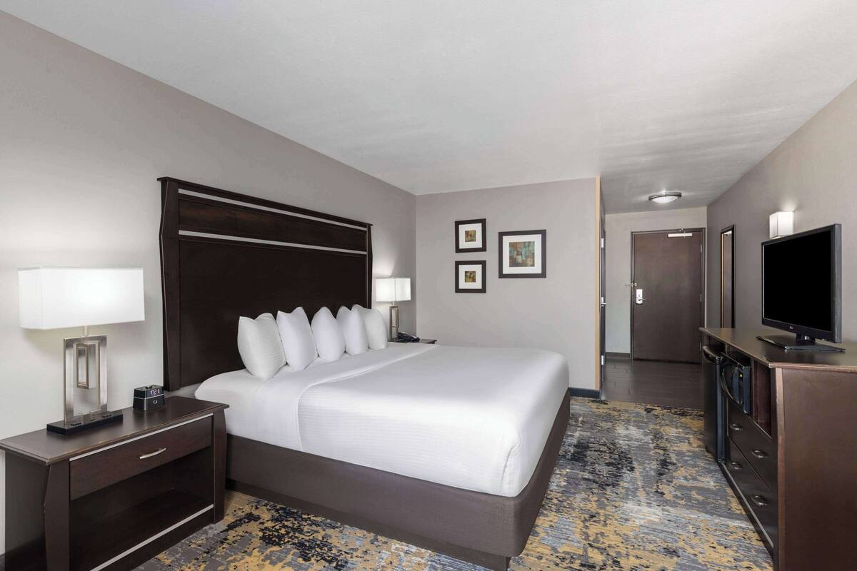 Een hotelkamer met een groot bed, een televisie, een bureau met een lamp en een dressoir.