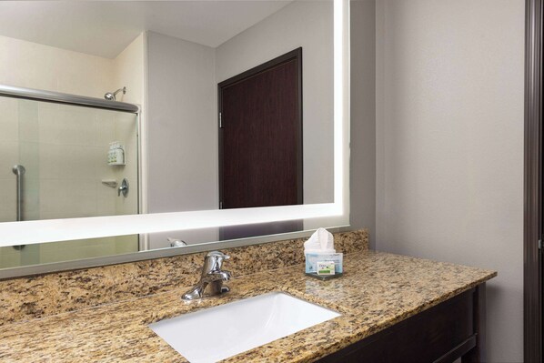 Un baño con encimera de granito, lavamanos blanco, espejo y puerta.