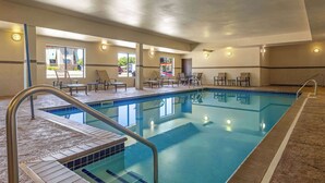 A swimming pool with a tiled deck, lounge chairs, and a sunroof.