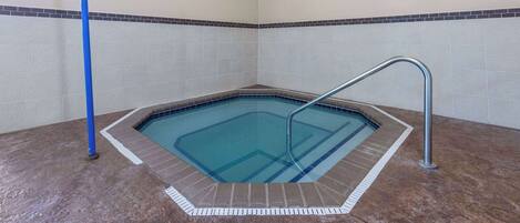 A small indoor swimming pool with a metal ladder and a blue pole, surrounded by tiled walls and a brown floor.