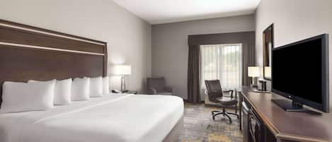 A hotel room with a large bed, a desk with a flat-screen TV, a chair, and a desk lamp.