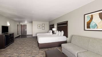 A hotel room with a large bed, a sofa, a television, and a carpeted floor.