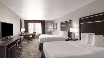 A hotel room with two beds, a desk with a television, a chair, and a lamp.
