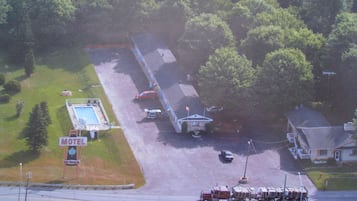 An aerial view of a motel with a swimming pool, a fire truck parked in front, and a large truck with cargo.