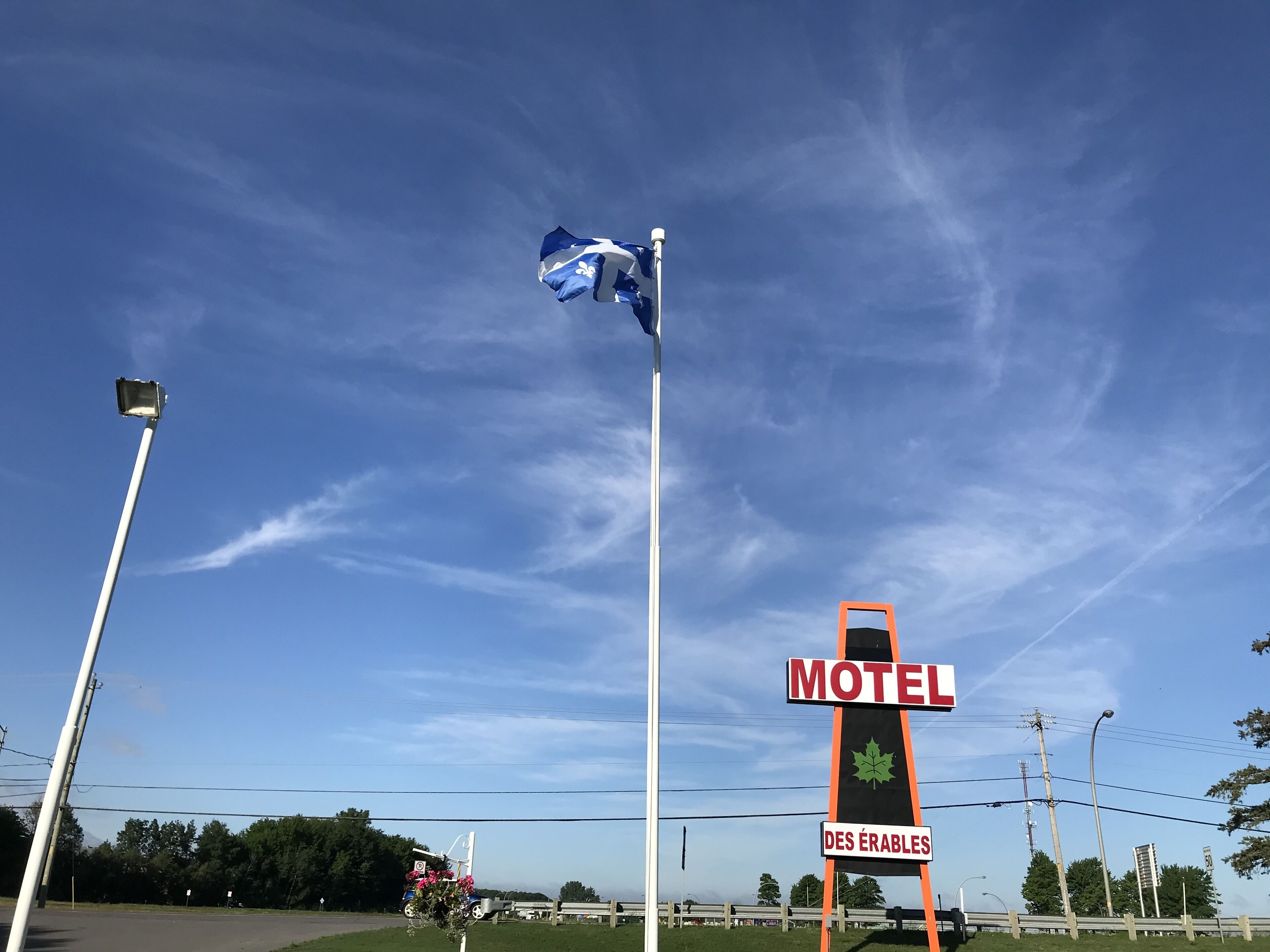 Segnaletica di motel con una bandiera, un lampione e cielo azzurro.