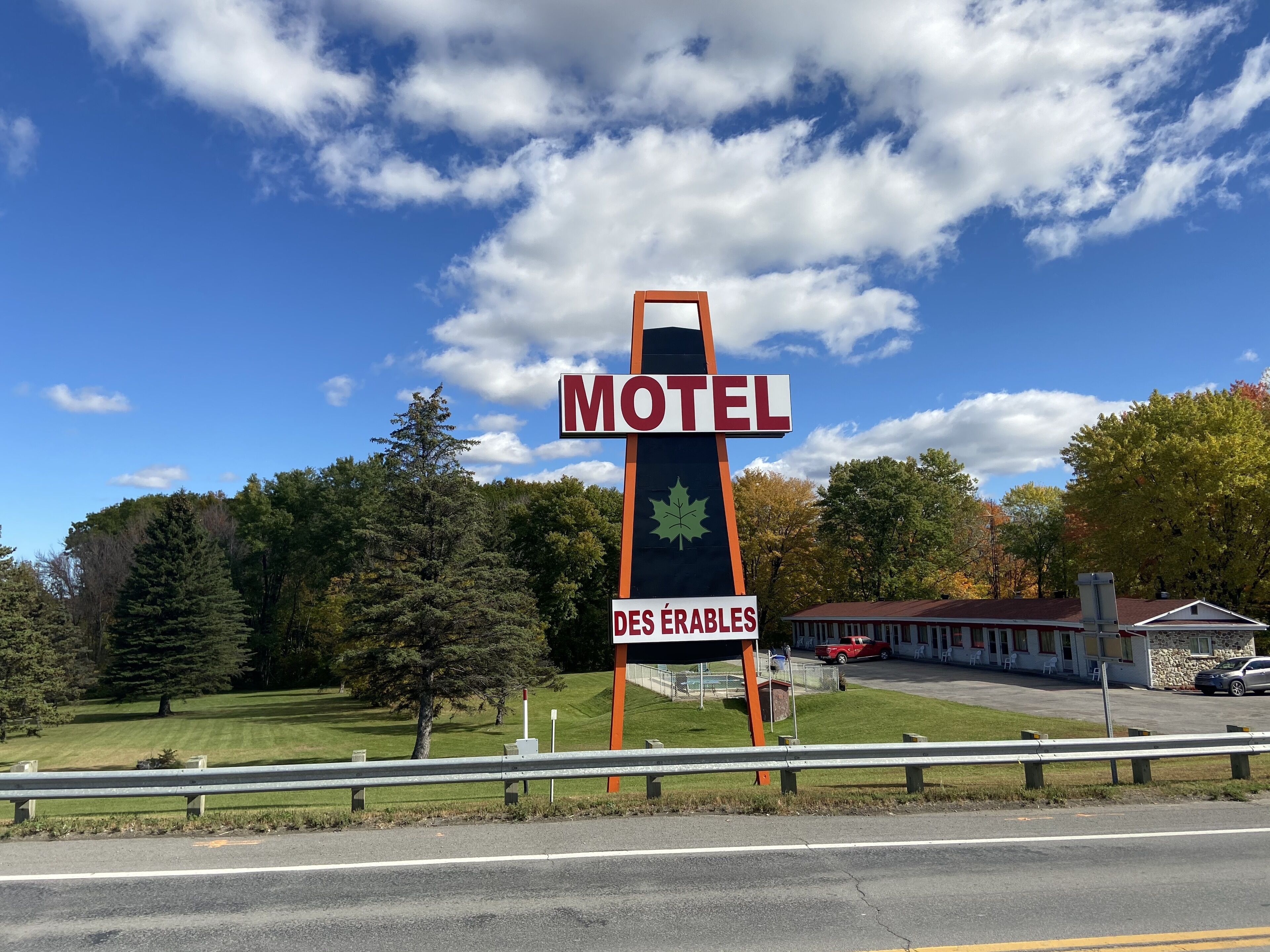 A motel sign with a maple leaf emblem, a red roof, and a parking lot with a few cars.
