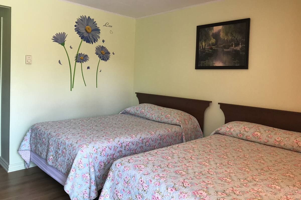 A room with two beds, floral bedding, a wall with a painting, and a wall decoration of flowers and butterflies.