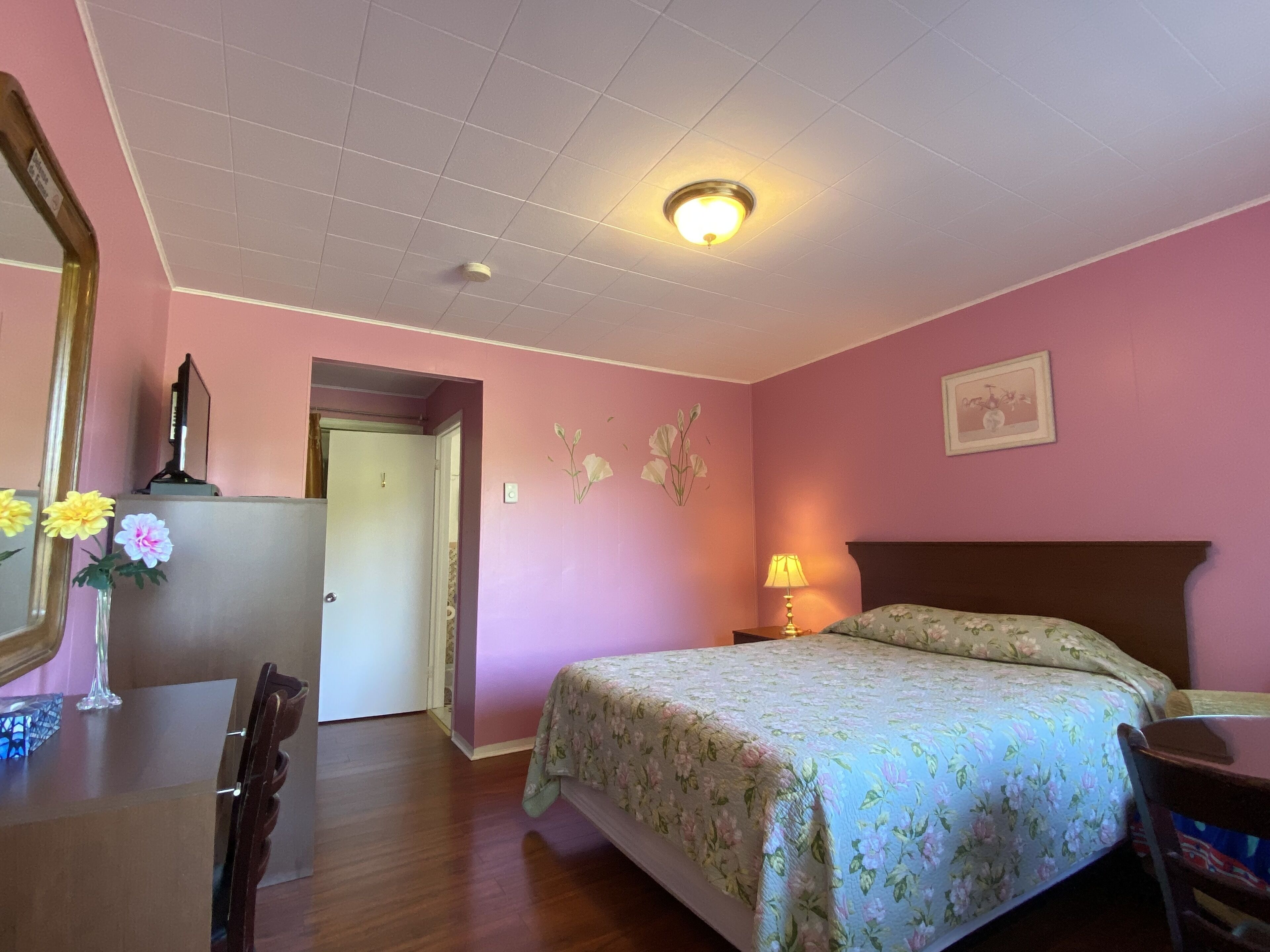 A bedroom with a bed, a desk, a chair, a mirror, and a door.