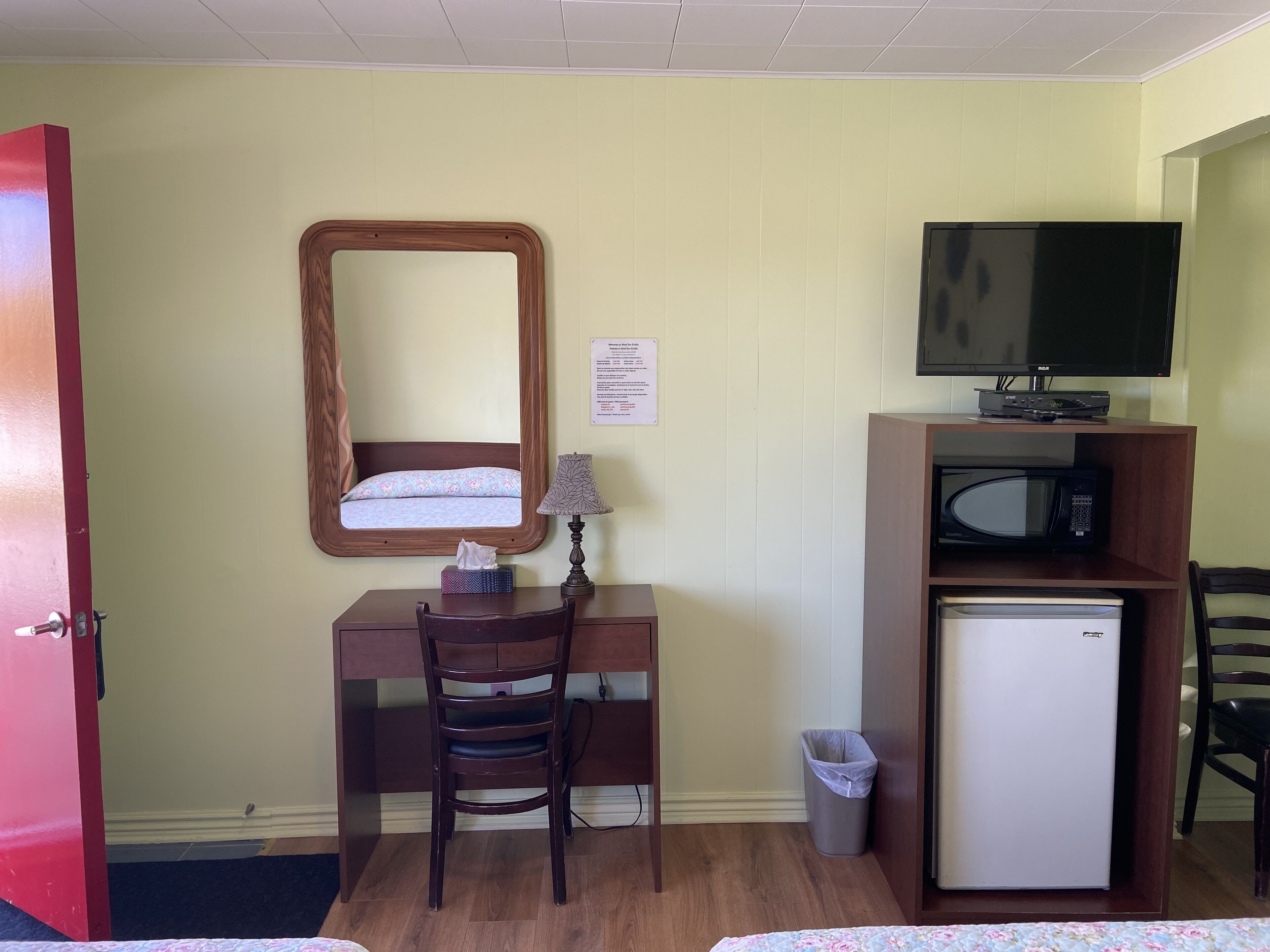 A hotel room with a wooden desk, a chair, a television, a microwave, and a small refrigerator.