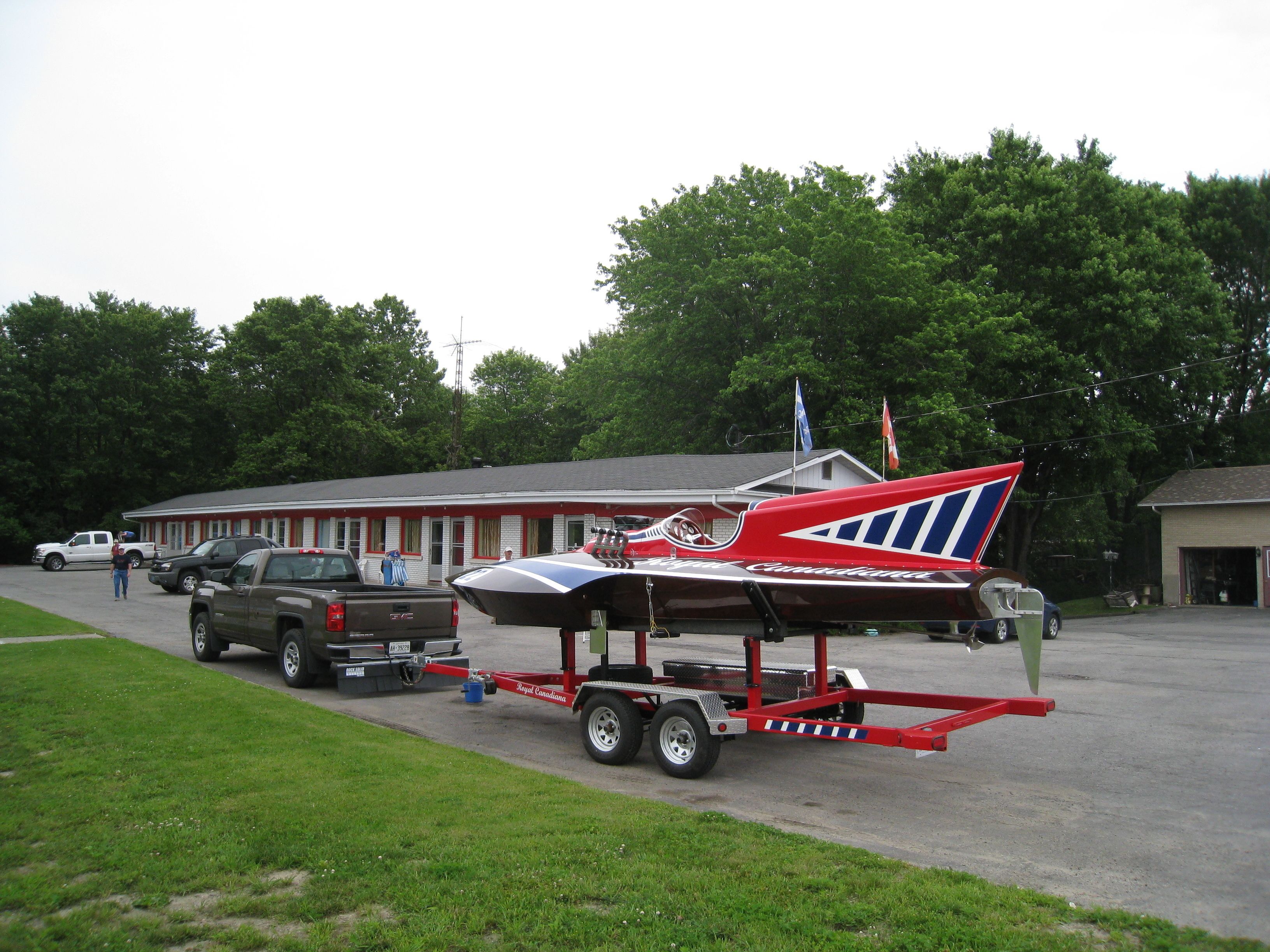 A trailer with a boat, parked in front of a building with a red and white facade.